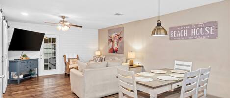 A dining area with a table set for four, a sofa, and a television in the background.
