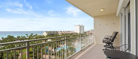 A balcony with a view of the ocean, a pool, and a building in the background.