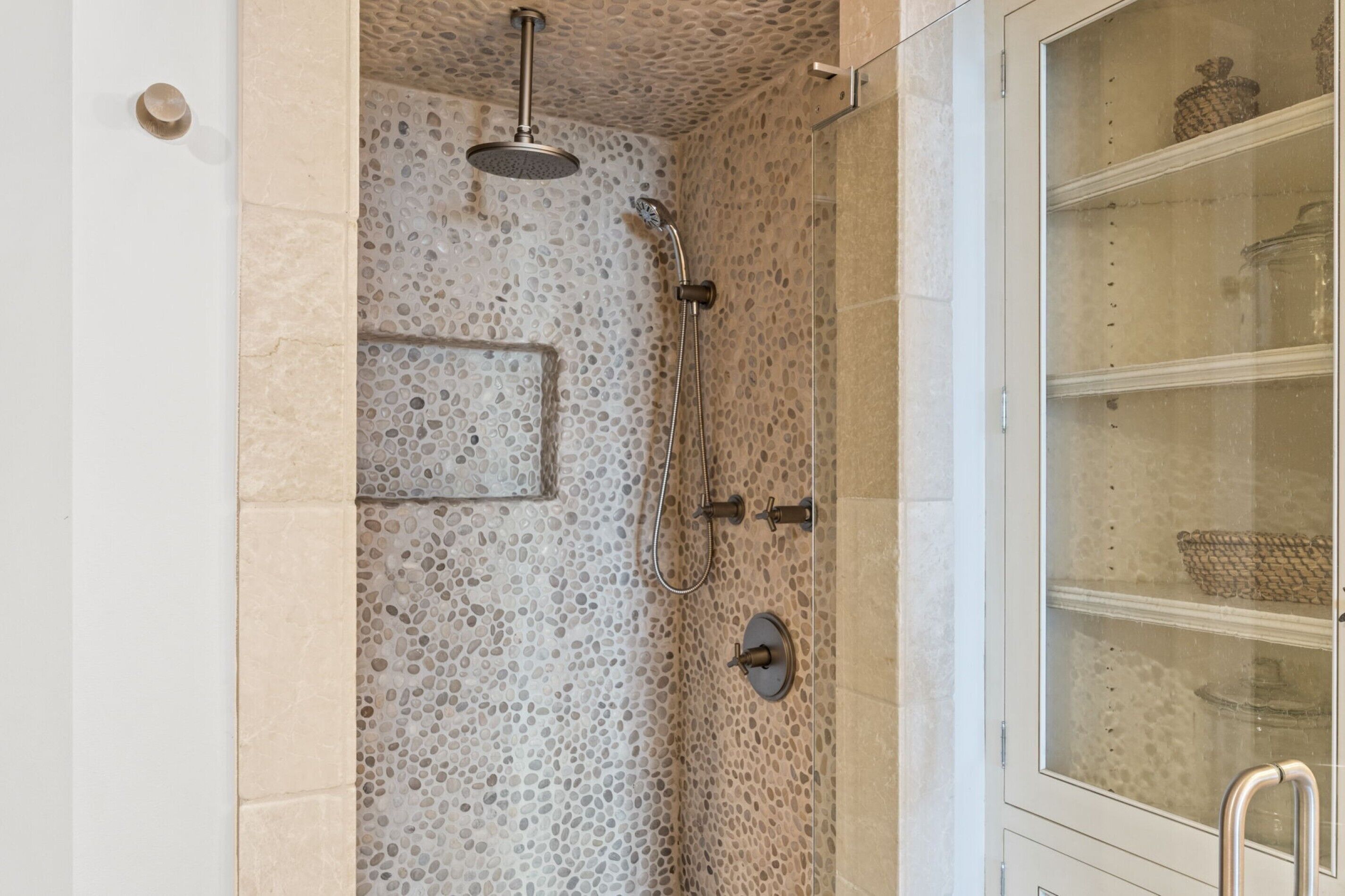 Une douche équipée d’un pommeau de douche à effet pluie, d’un pommeau de douche à main et d’une paroi en verre avec des étagères.