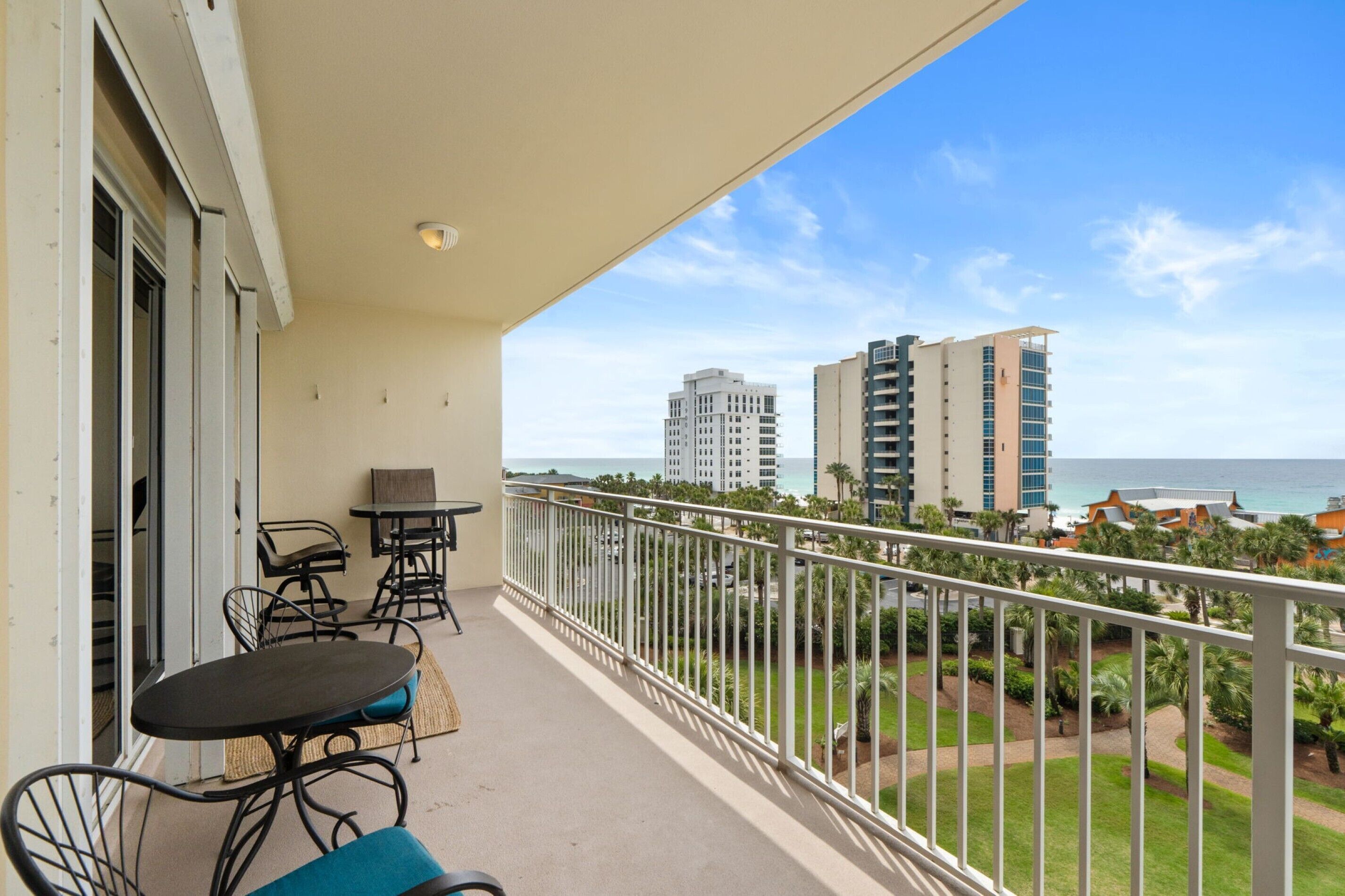 A balcony with a table and chairs, a view of the ocean, and buildings in the background.