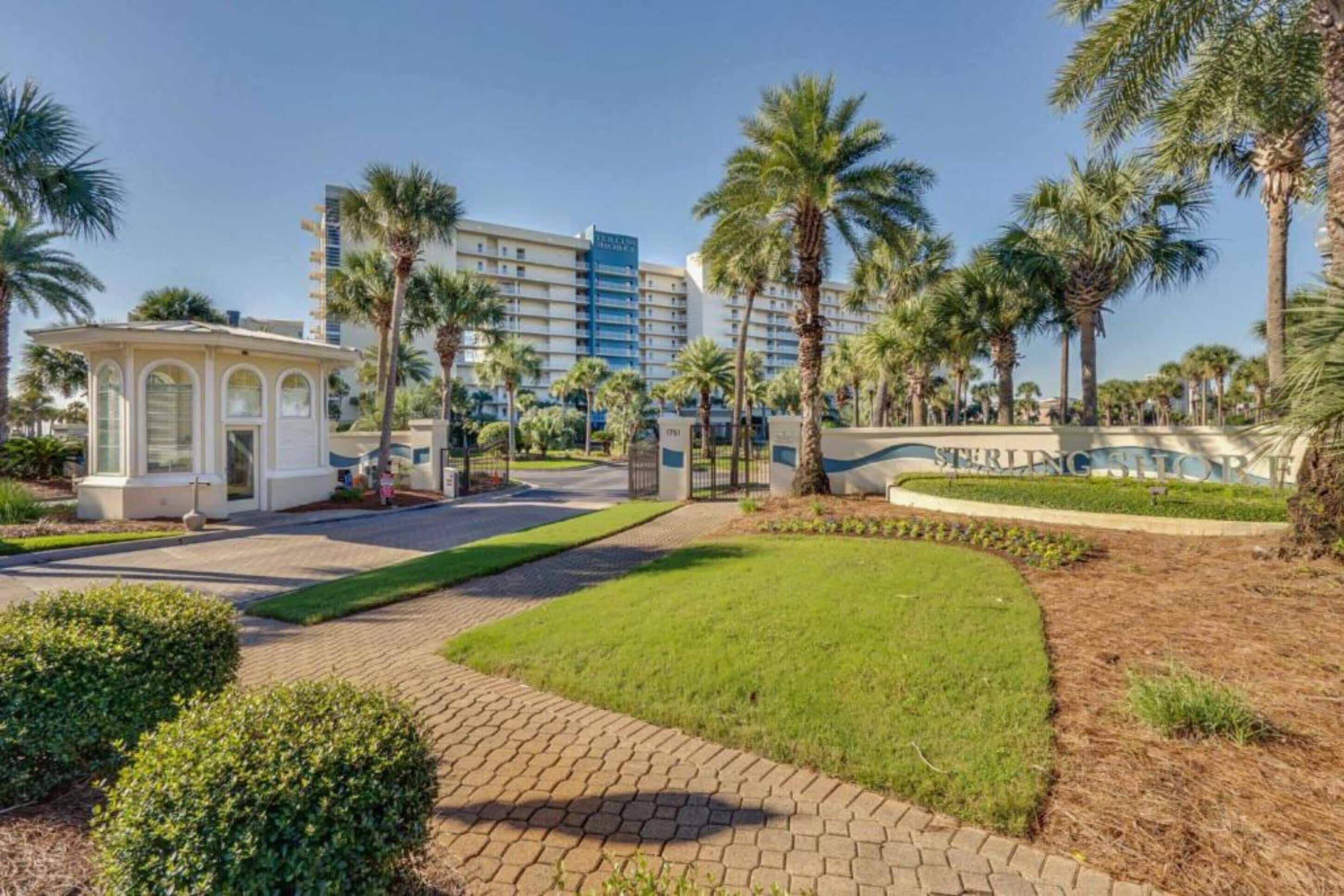 A hotel entrance with a gated driveway, palm trees, and a building with a sign.