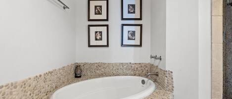 A bathroom with a stone-tub, framed pictures on the wall, and a towel rack.