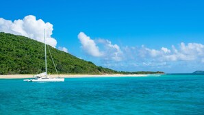 A white sailboat on turquoise waters with a sandy beach and a forested hill in the background. - Oceanfront, Remodeled 2BR- 2 King Size Beds / 2BA Condo at Ocean's View (Christiansted)