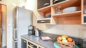 A kitchen with a stainless steel refrigerator, a coffee maker, and a fruit basket on the counter. - Oustaù des Carmes intra-muros (Avignon)