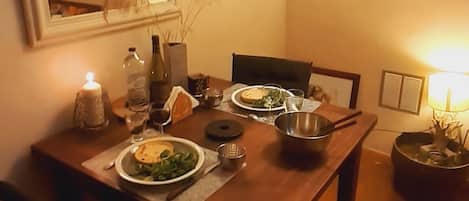 A dining area with a wooden table set for two, a mirror above the table, and a lamp on the right.