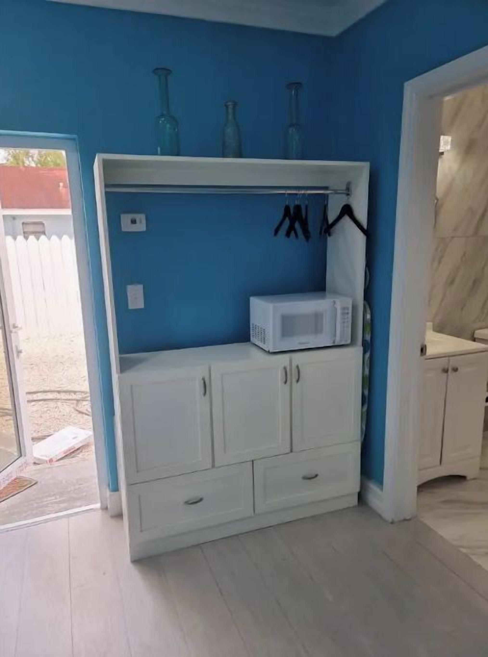 Ein Zimmer mit einem weißen Kleiderschrank, einer Mikrowelle und einem Regal mit blauen Flaschen.