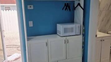 A room with a white wardrobe, a microwave, and a shelf with blue bottles.