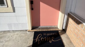 A pink door with a doormat that reads "It's good to be home." - Low FEES! King Beds.  Free Parking, Wi-Fi, & Coffee (Westworth Village)