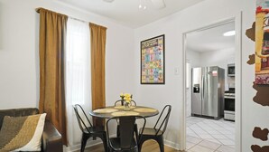 A dining area with a round table, black chairs, and a vase with yellow flowers. A brown curtain and a wall-mounted alphabet poster are visible. - Low FEES! King Beds.  Free Parking, Wi-Fi, & Coffee (Westworth Village)