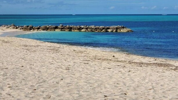 A sandy beach with a rocky breakwater extending into the ocean. - Elegance & Grace in Nassau contemporary beauty (Nassau)