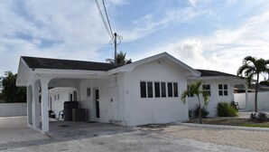 A single-story white building with a covered entrance and a small garden area with palm trees. - Elegance & Grace in Nassau contemporary beauty (Nassau)