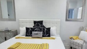 A bedroom with a bed, a ceiling fan, two bedside tables, a chair, and two mirrors on the walls. - Elegance & Grace in Nassau contemporary beauty (Nassau)