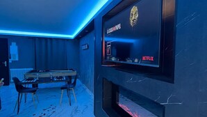 Un salon moderne doté d’un grand téléviseur à écran plat fixé au mur, d’une table de billard et d’une cheminée.