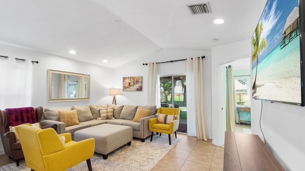 A modern living room with a sectional sofa, a yellow armchair, and a wooden coffee table. - Pet-Friendly Jupiter Home • Game Room • Central (Jupiter)