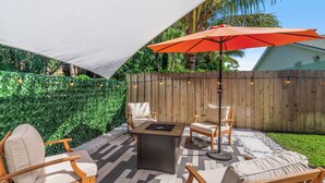 An outdoor patio with a fire pit table, wooden chairs, and an orange umbrella. - Pet-Friendly Jupiter Home • Game Room • Central (Jupiter)