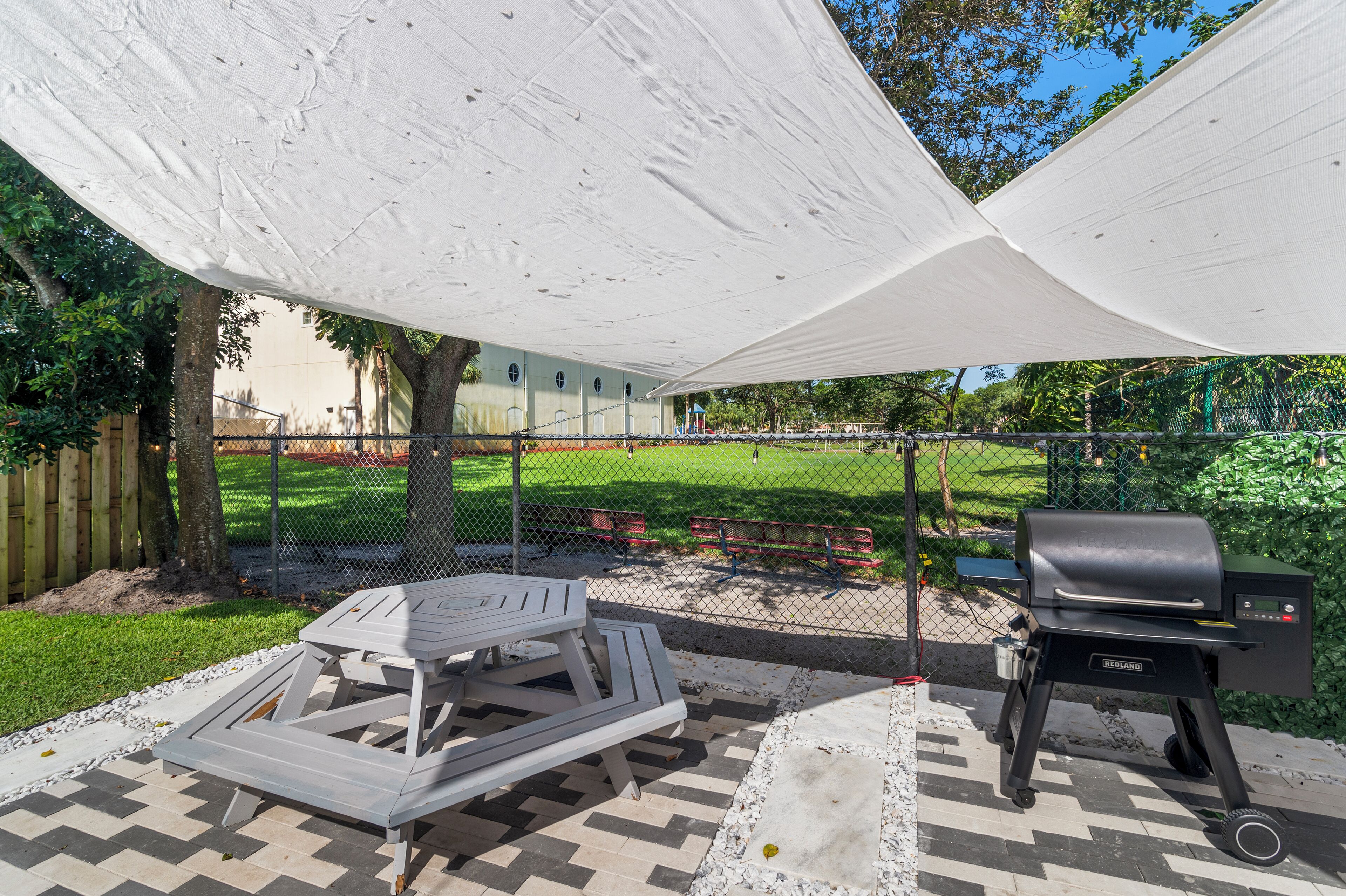 A patio with a grill, picnic table, and shade canopy.