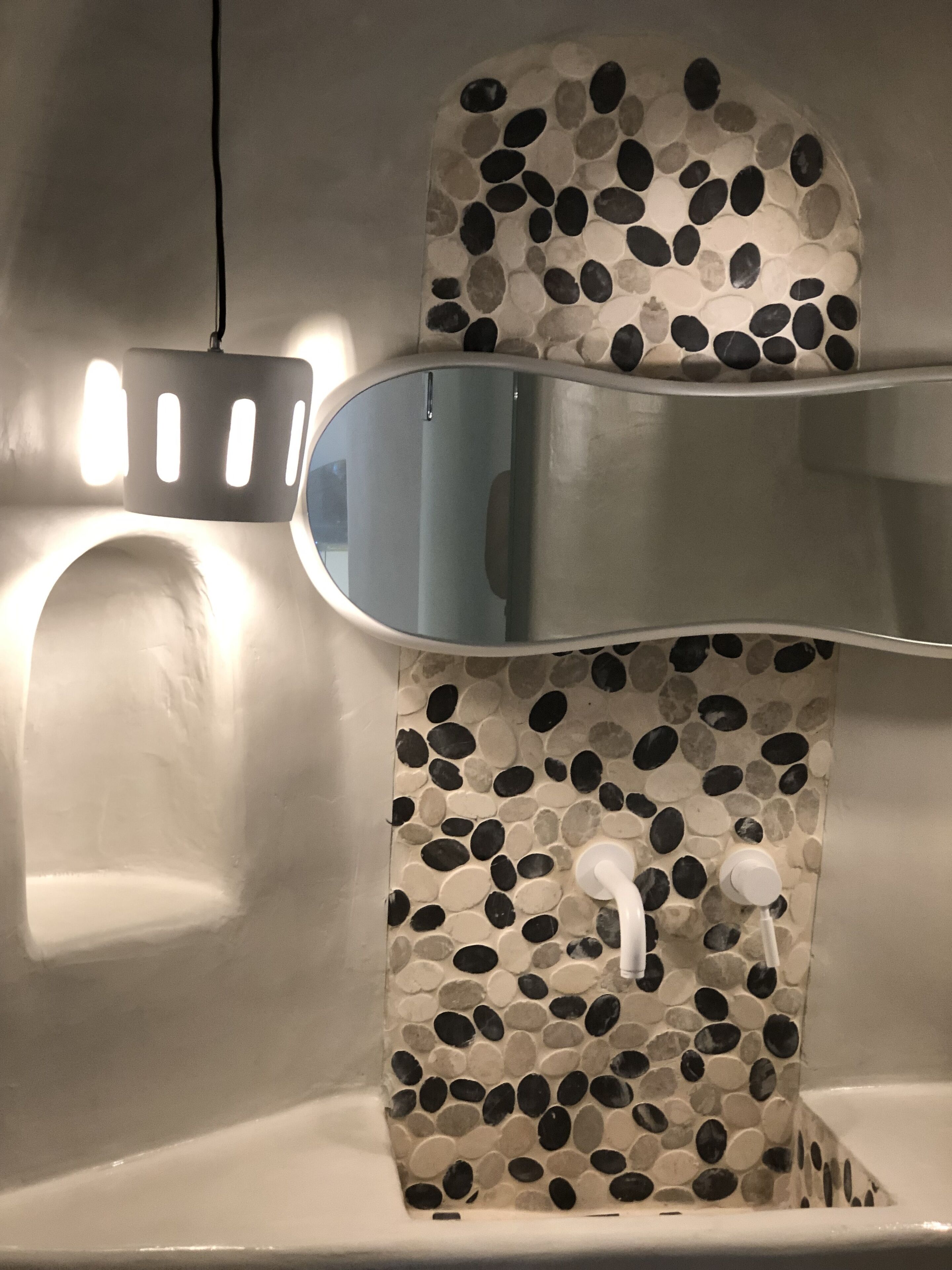 A bathroom with a pebbled mosaic wall, a modern faucet, and a pendant light.