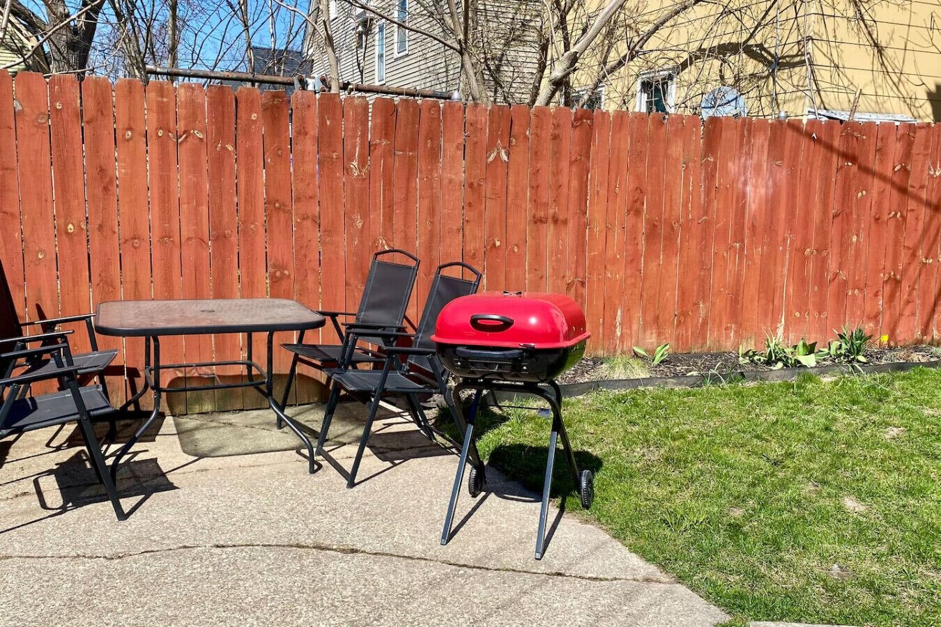 A patio with a table, chairs, and a red grill.