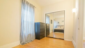 A bedroom with a wooden floor, a black dresser, a mirrored closet door, and a polka dot curtain. - Elmwood Village 2BR Apt •Sleeps 8• Walk to Dining (Buffalo)