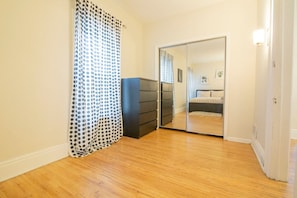 A bedroom with a wooden floor, a black dresser, a mirrored closet door, and a polka dot curtain. - Elmwood Village 2BR Apt •Sleeps 8• Walk to Dining (Buffalo)