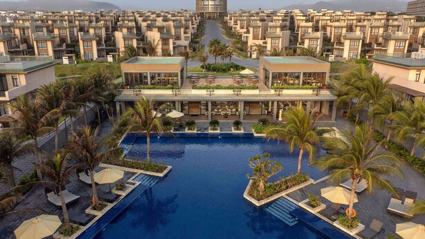 A resort with a central swimming pool, palm trees, and a view of a mountain range. - Wyndham Garden Cam Ranh Resort (Cam Lam)