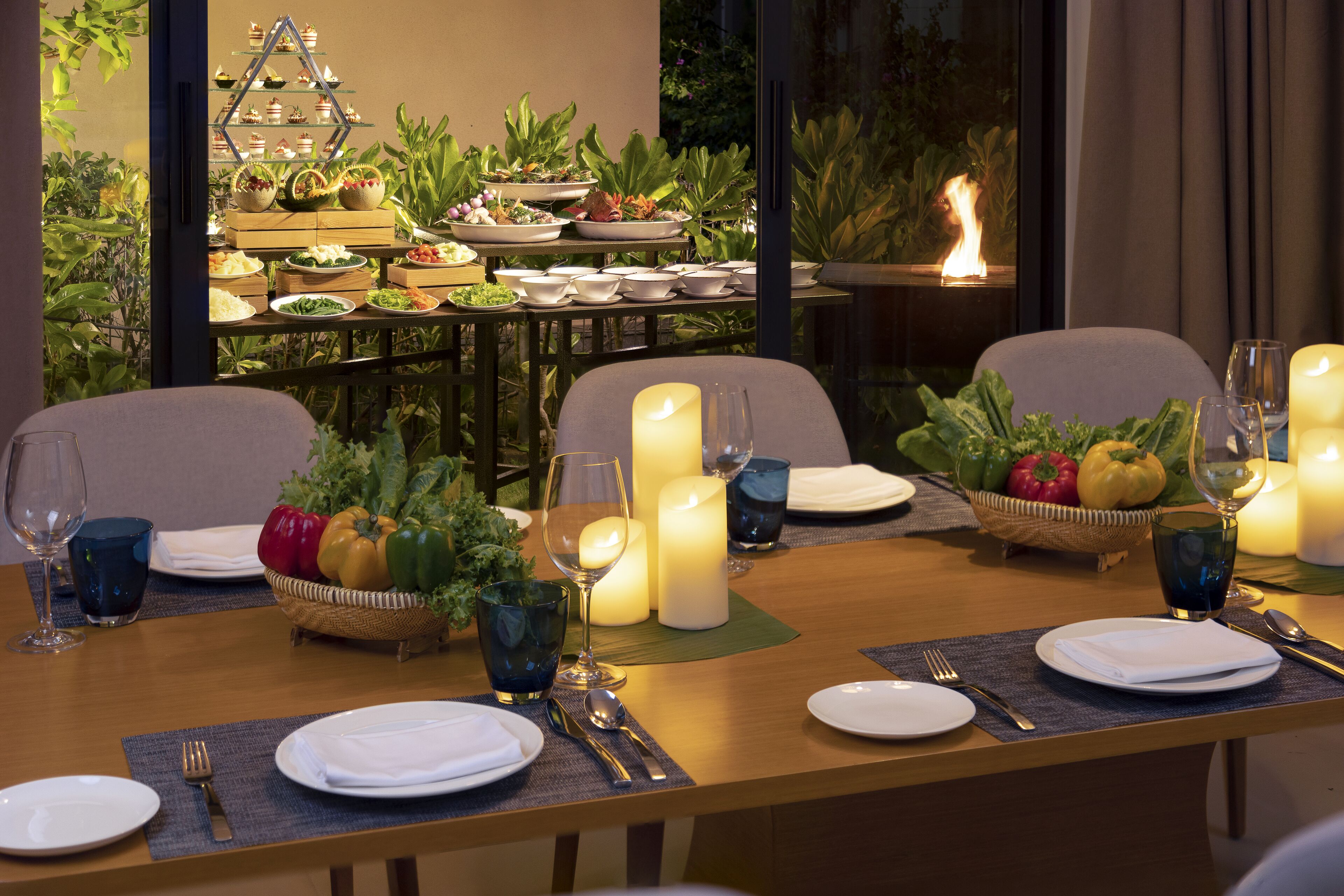 Une table à manger joliment dressée, avec des bougies, des assiettes, des couverts et un panier de fruits.