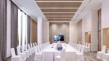 Una sala de conferencias moderna con una larga mesa, sillas blancas y una pantalla grande.