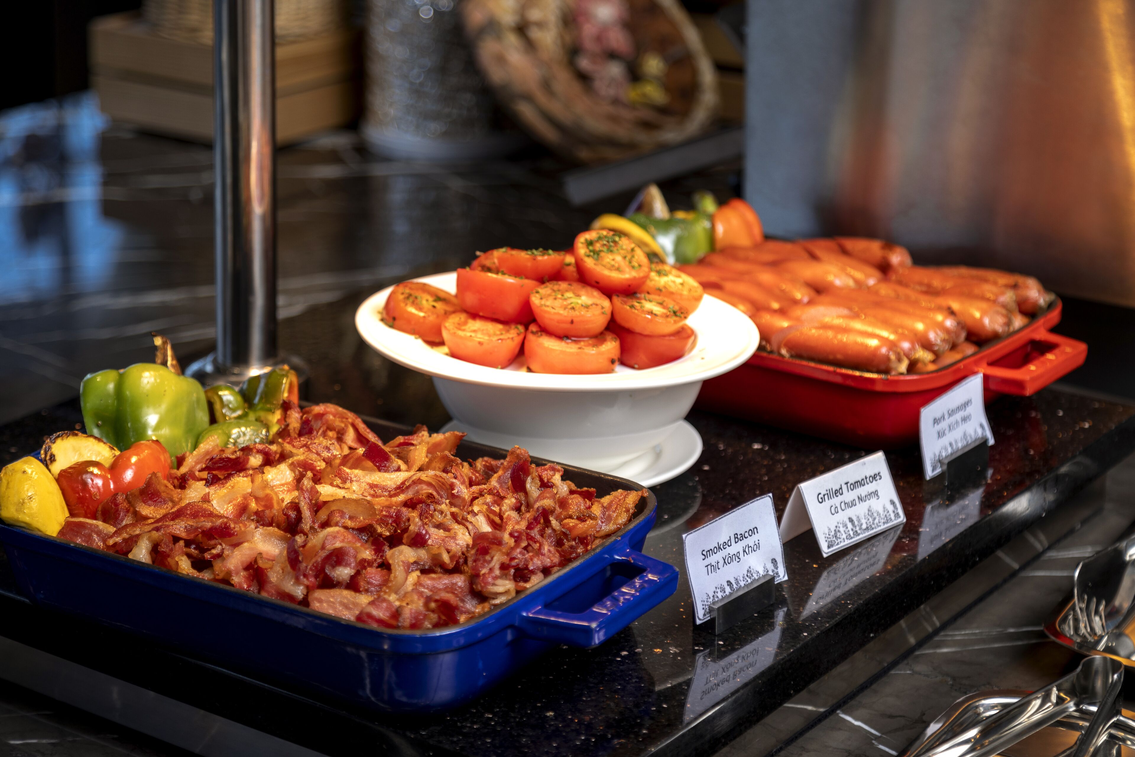 Un bufé con diferentes opciones de comida, incluyendo tocino, tomates a la parrilla y salchichas.
