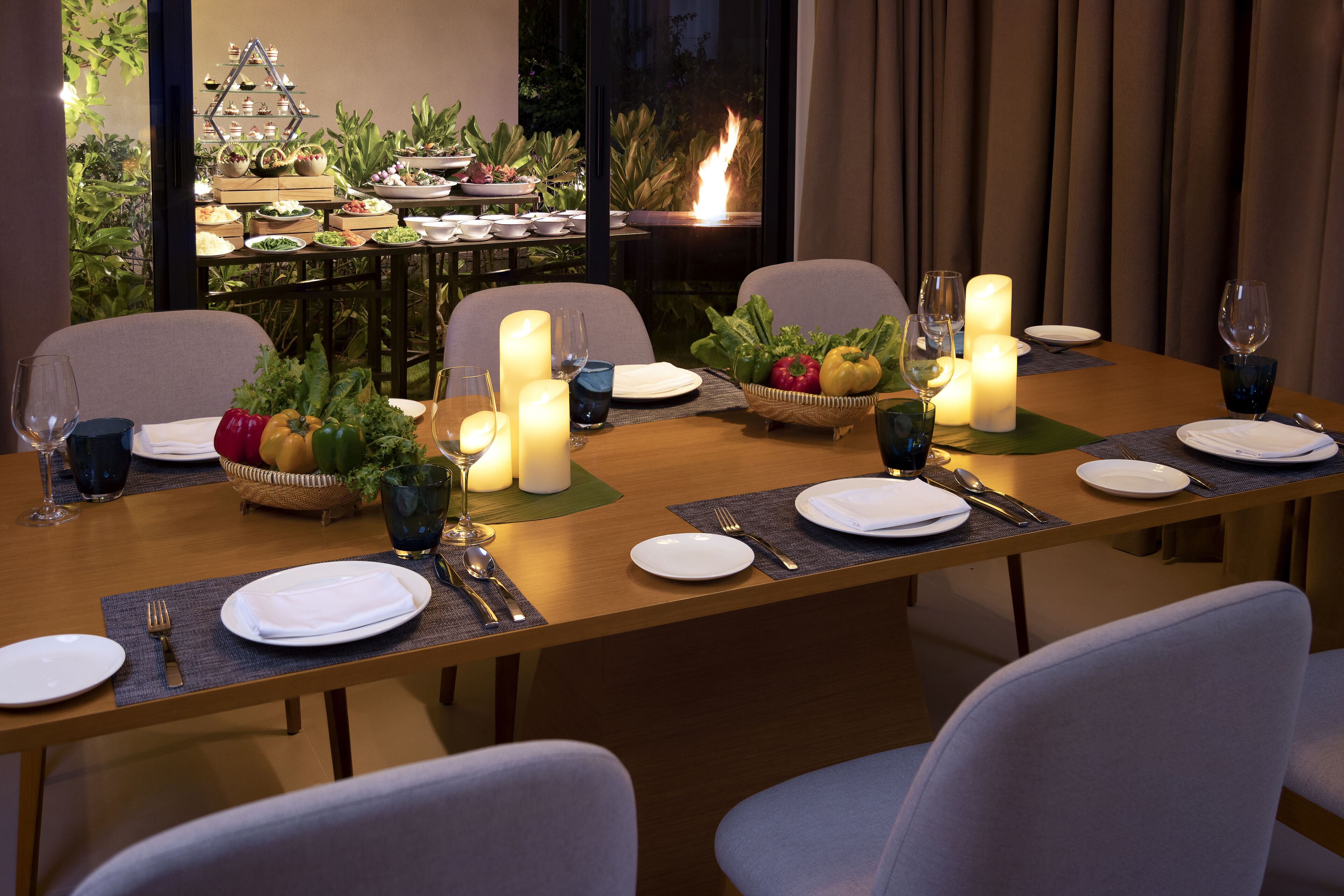 A dining table set for four with candles, plates, cutlery, and a fruit basket.