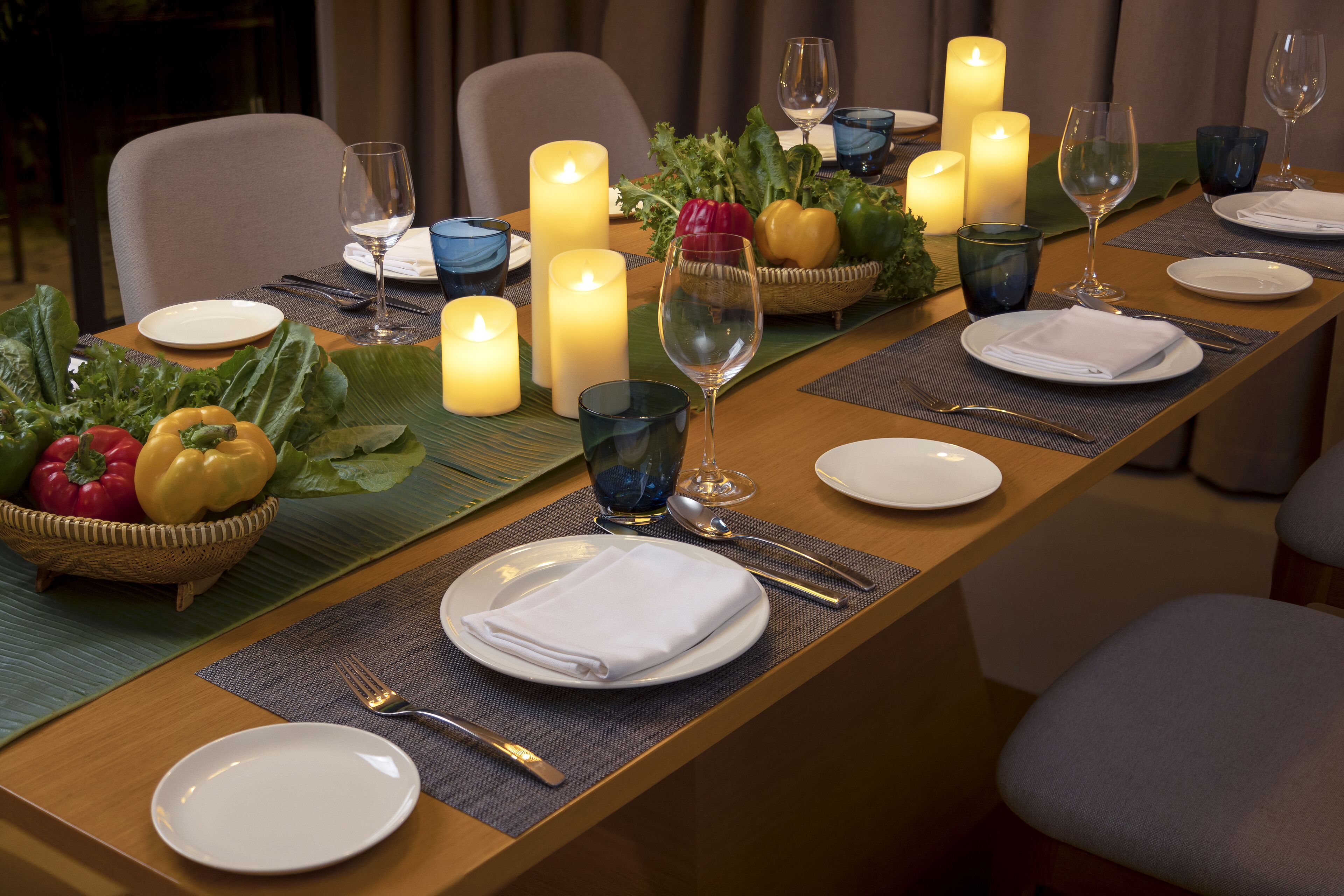 A dining table set with candles, plates, glasses, and a fruit basket.