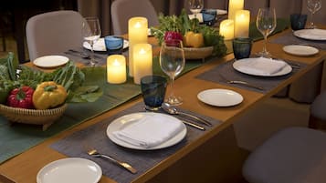 A dining table set with candles, plates, glasses, and a fruit basket.