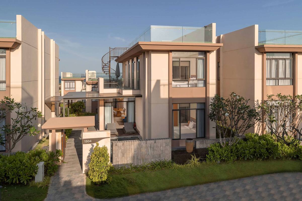 A modern residential building with a glass balcony, a staircase, and a well-maintained garden.