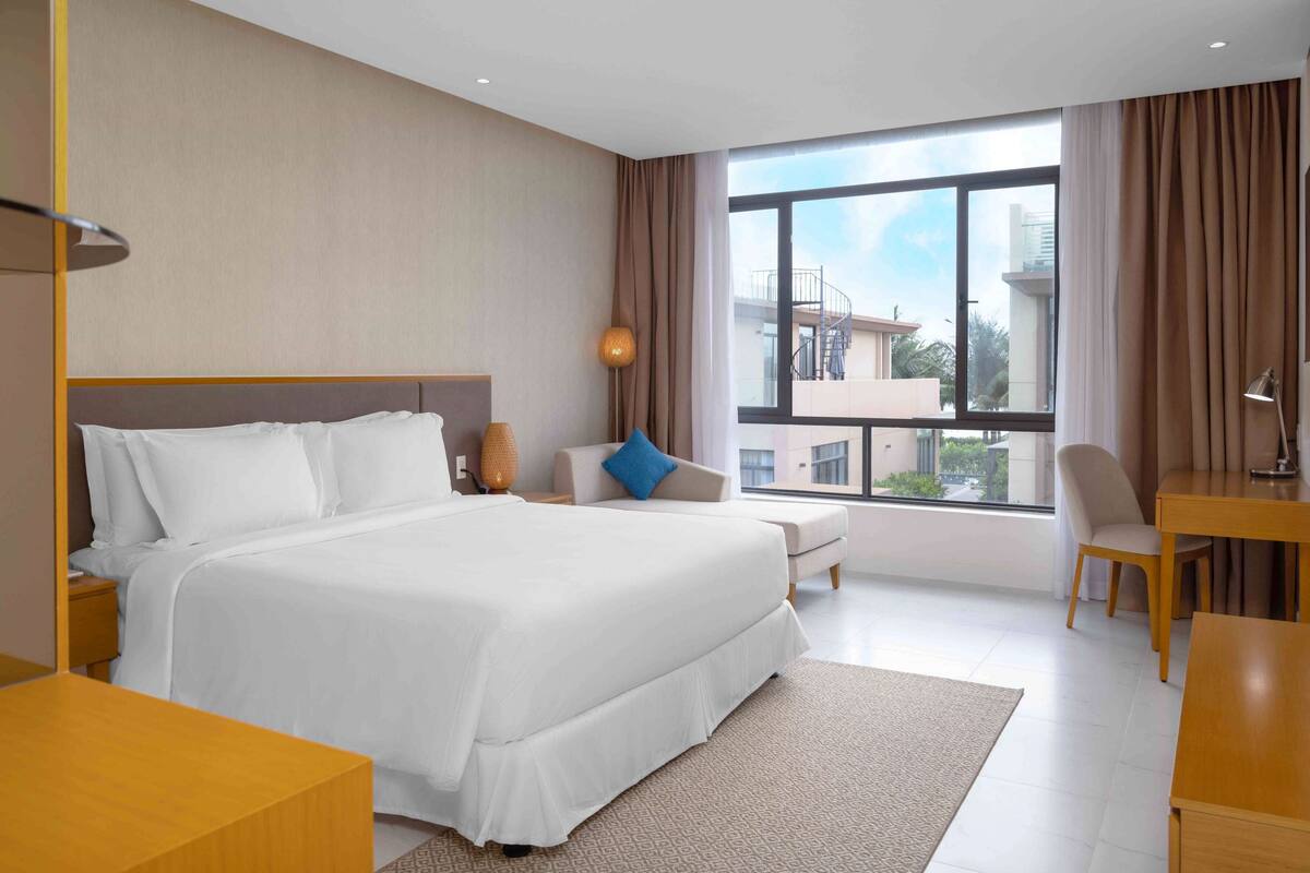 A modern hotel room with a large bed, a desk, and a view of the city.