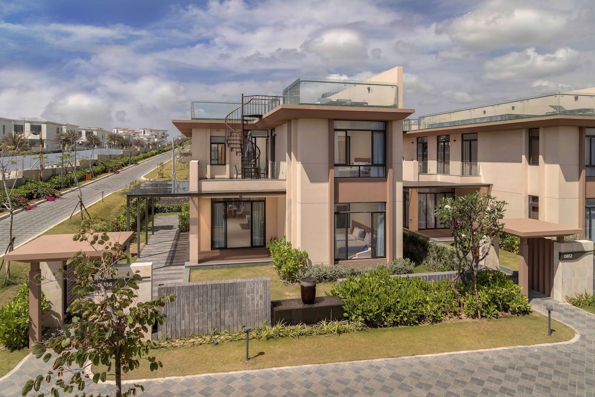 A modern residential building with a two-story structure, a glass balcony, and a paved driveway.