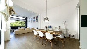 A modern living room with a sofa, dining table, and chairs. There is a TV in the background, and artwork on the wall.