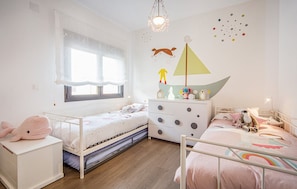 A child's bedroom with two beds, a dresser, a window with curtains, and wall decorations.
