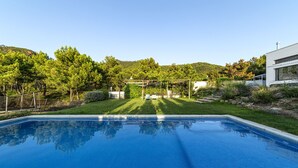 A rectangular swimming pool with clear blue water, surrounded by a well-maintained lawn and trees.