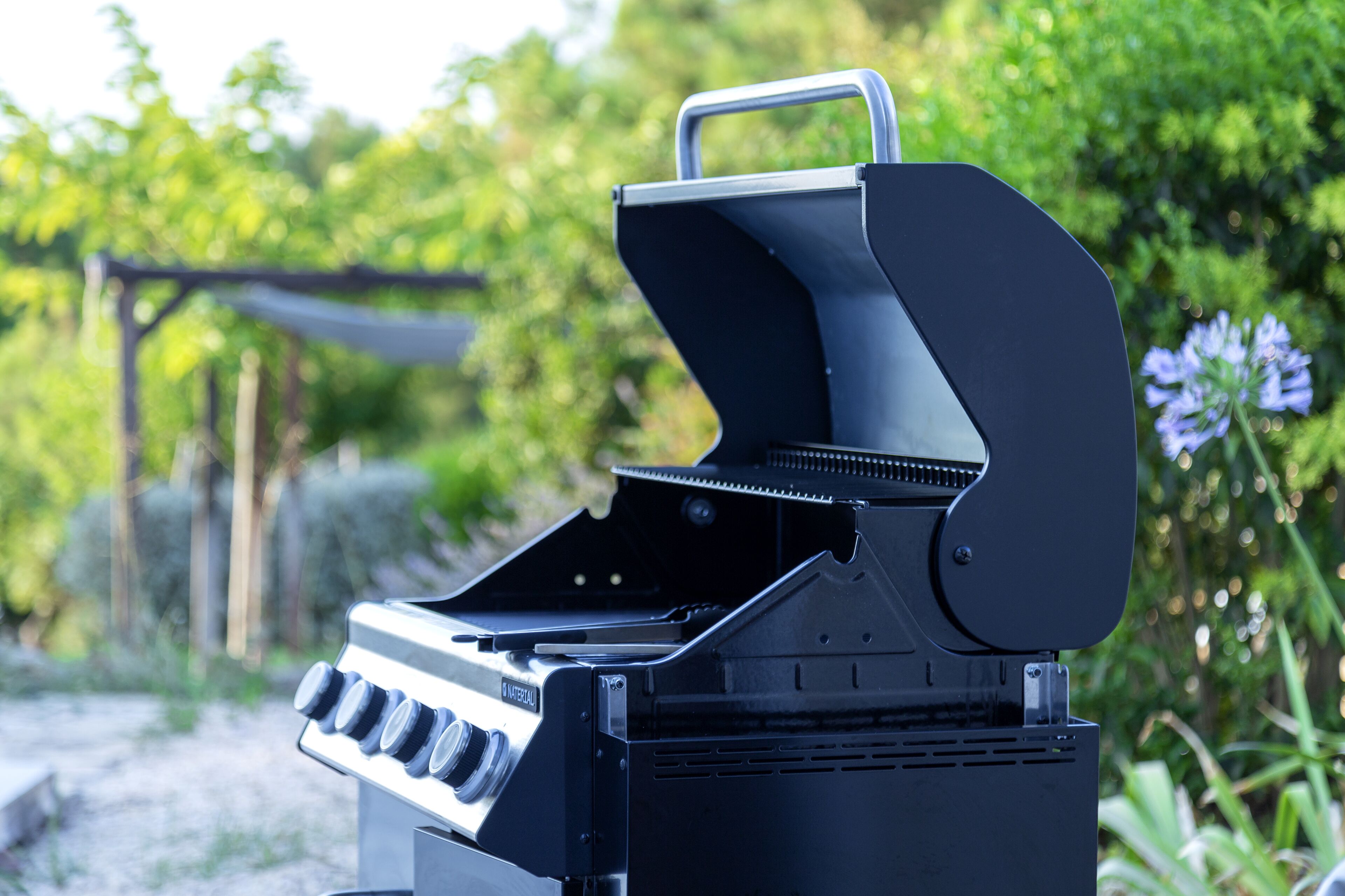 Un barbecue noir, doté d’une poignée et de boutons de contrôle, installé à l’extérieur, avec de la verdure en arrière-plan.