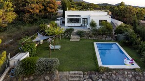 A modern house with a swimming pool, surrounded by a well-maintained garden and a view of hills.