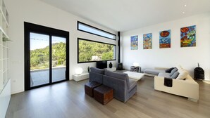 A modern living room with a large window, a grey sofa, a white sofa, and colorful artwork on the wall.