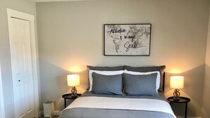 Un dormitorio con una cama, dos mesitas de noche, un mapa en la pared y una puerta.