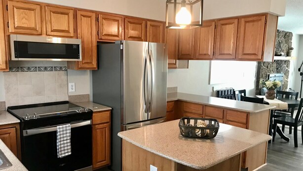 Una cocina moderna con armarios de madera, electrodomésticos de acero inoxidable, encimera de granito y una isla central.