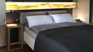 Une chambre moderne avec un grand lit, une table de chevet et un téléviseur fixé au mur.