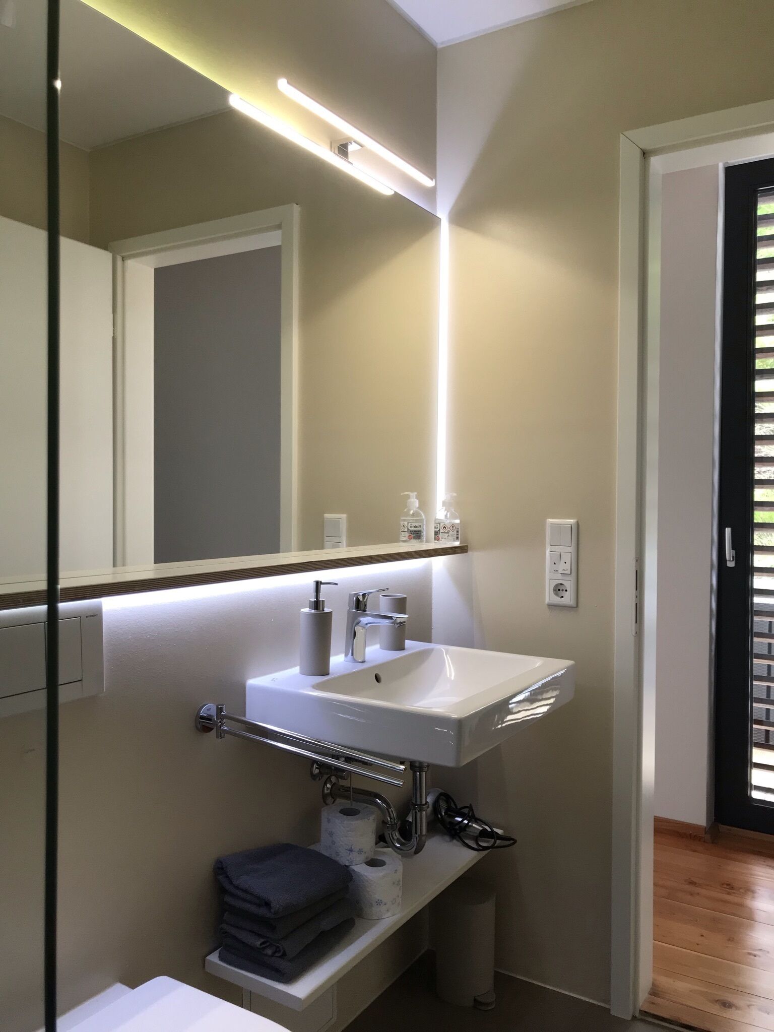 Ein modernes Badezimmer mit einem weißen Waschbecken, einem Spiegel und einem Handtuchhalter.