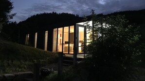 Une maison moderne avec une entrée dotée d’une porte en verre, entourée d’une zone boisée.