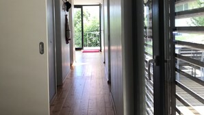 Un couloir doté d’un plancher en bois, de murs blancs et d’une porte en verre donnant sur un espace extérieur agrémenté d’un tapis rouge.