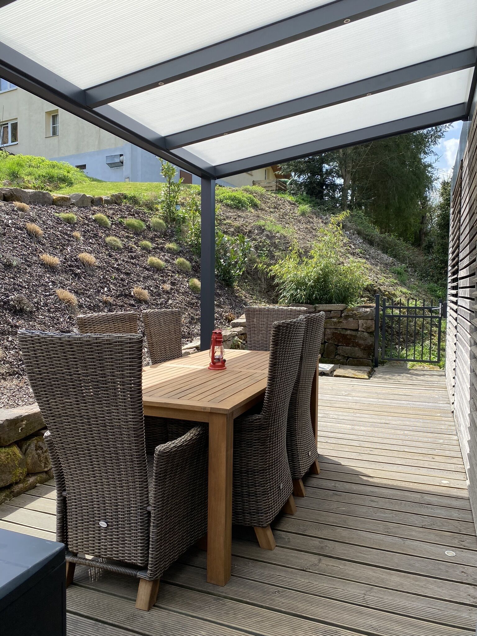 Eine Terrasss mit einem Holztisch, Korbstühlen, einem roten Laternen und Blick auf eine Hügelkette.
