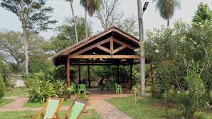 Ein hölzernes Pavillon mit einem Reetdach, umgeben von üppiger Vegetation und einem Kiesweg.