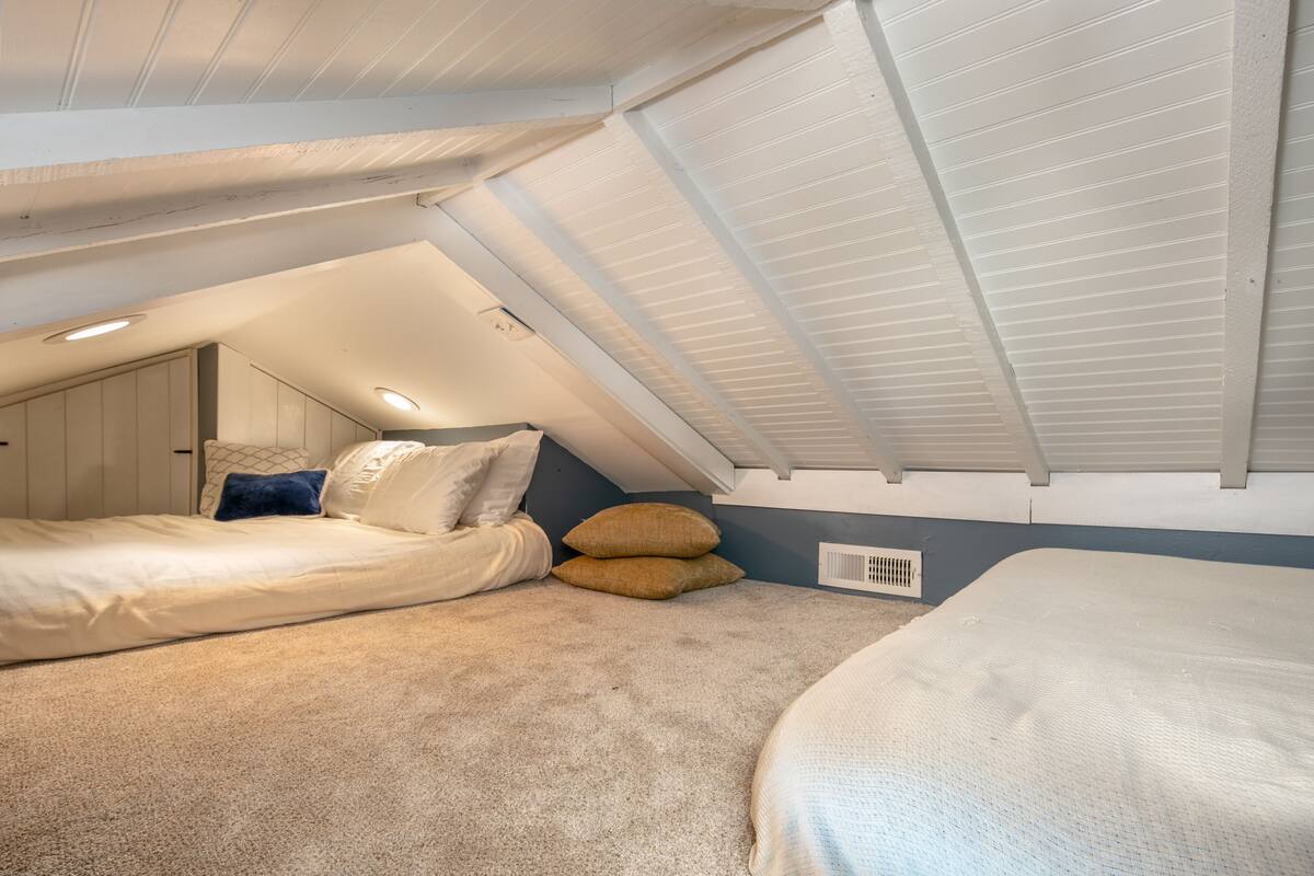 A bedroom with a sloped ceiling, two beds, and a window.