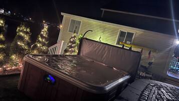 A hot tub with a digital control panel, a covered patio area, and a house with Christmas lights in the background.